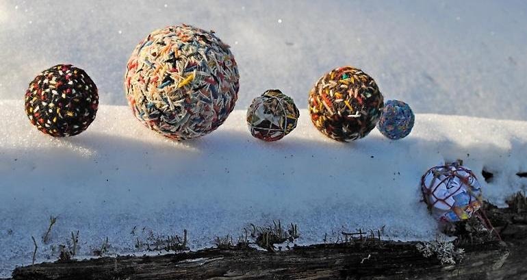 På en snöbeklädd stock ligger sex garnbollar i olika storlekar.