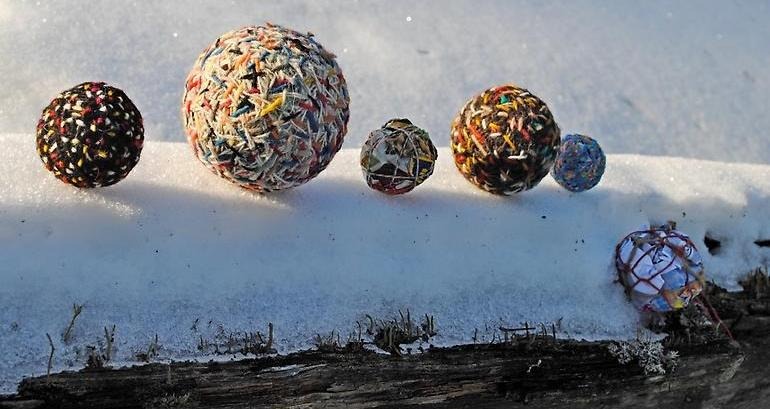 På en snöbeklädd stock ligger sex garnbollar i olika storlekar. 