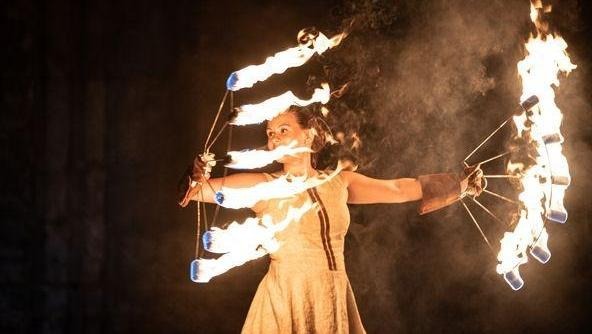 En kvinna står med sex brinnande facklor i vardera hand och snurrar dem runt. 
