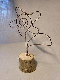 En blomma av metalltråd som står på en trädkloss.